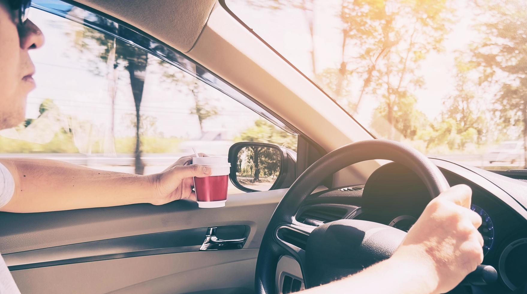 Man driving car using one hand while holding a coffee cup in other hand photo