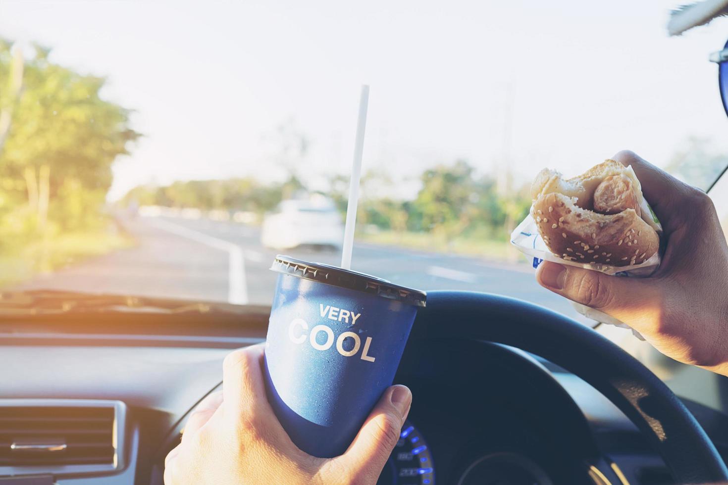 Man is dangerously eating hot dog and cold drink while driving a car photo
