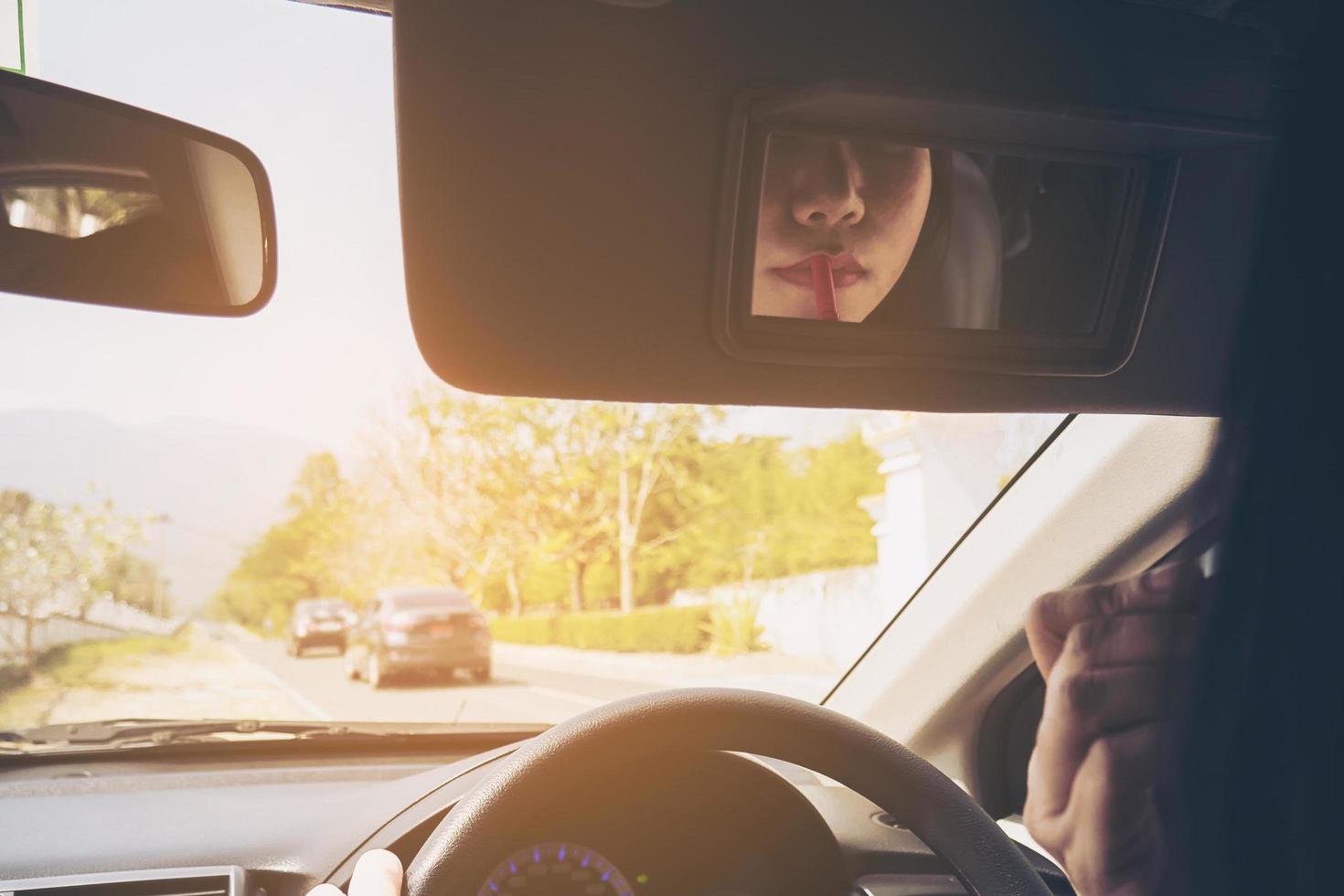 Woman making up her face using lipstick while driving car, unsafe behavior photo