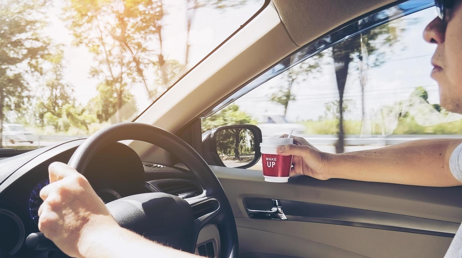 Man driving car using one hand while holding a coffee cup in other hand photo