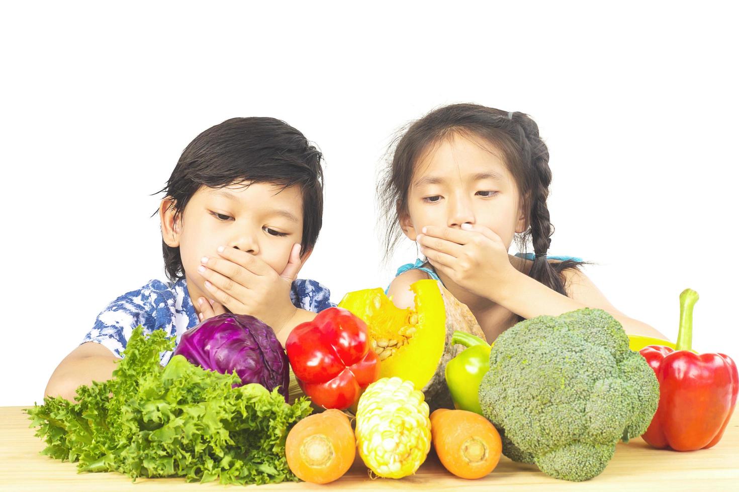 niño y niña asiáticos que muestran una expresión de desagrado con verduras frescas y coloridas aisladas sobre fondo blanco foto