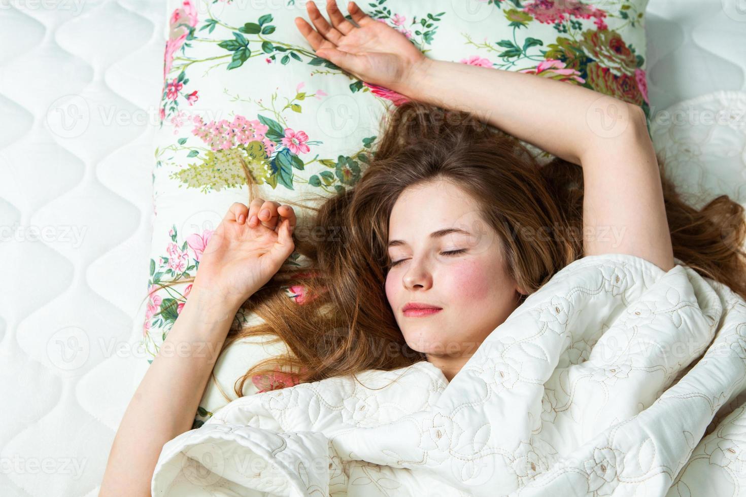 Girl sleeps in a white bed at home. Young woman sleeping in sleepwear on the white linen in bed at home, top view. photo