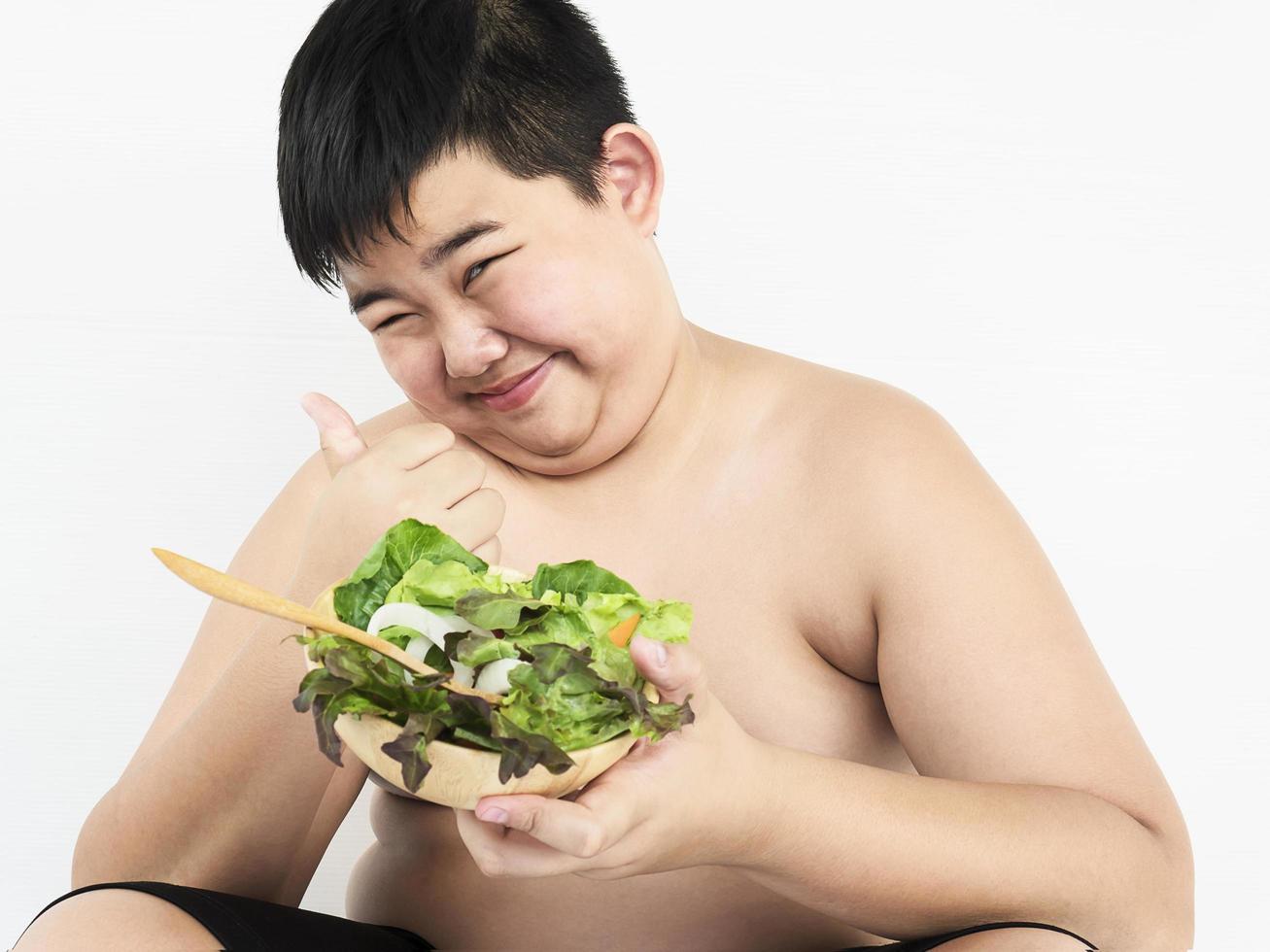 A fat boy is happily eating vegetable salad photo