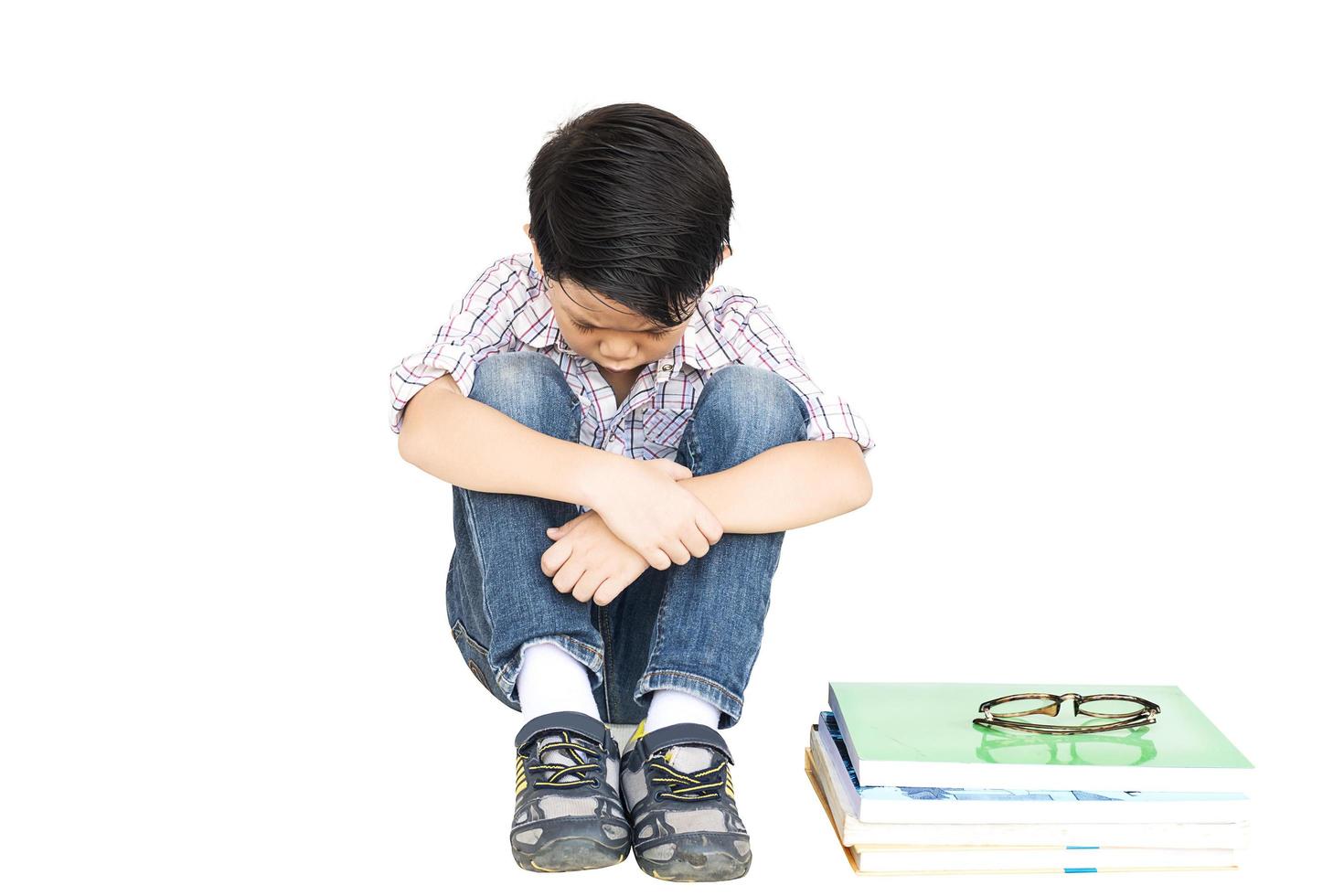 7 years old Asian boy is feeling sad with a pile of book isolated over white. photo