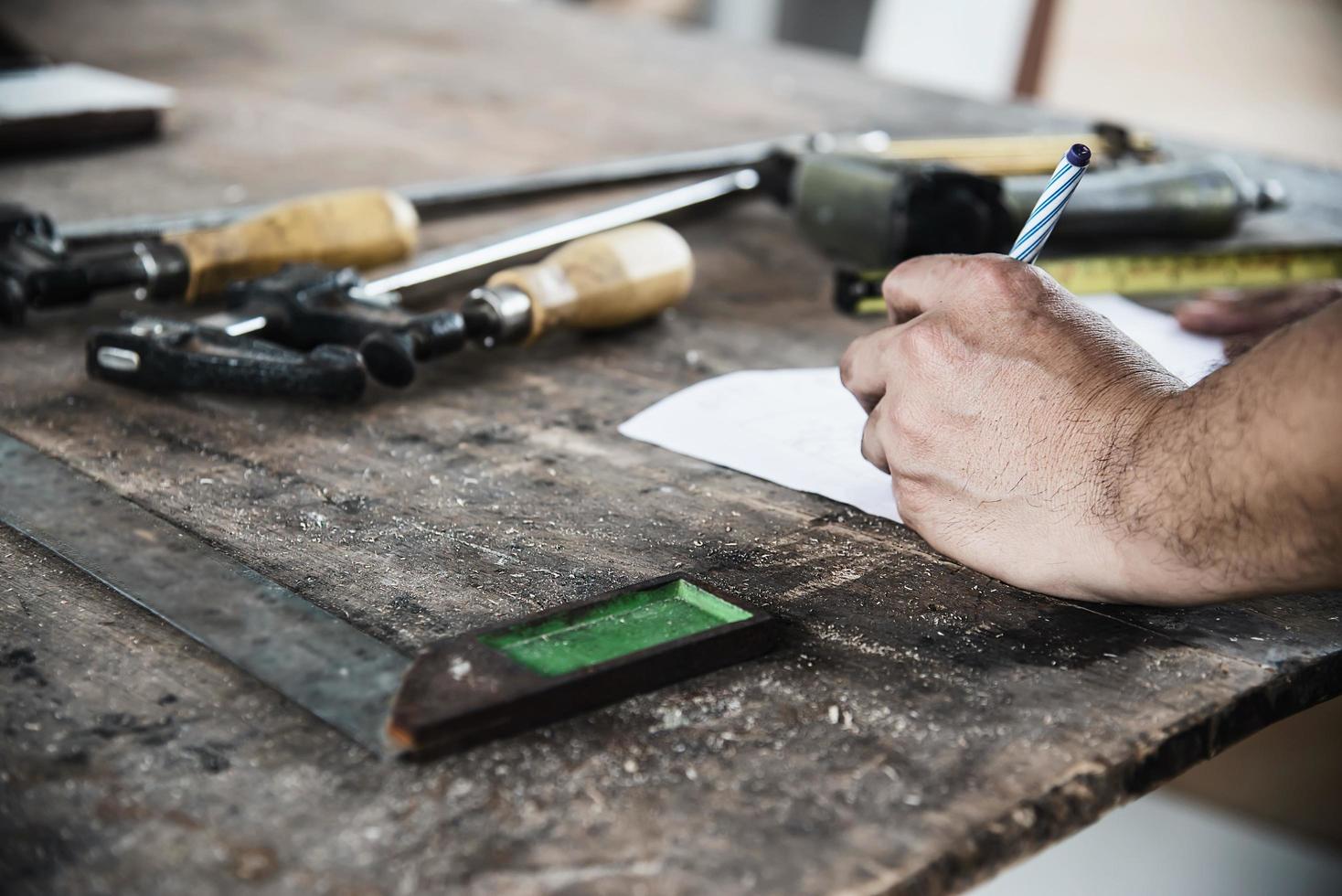 Carpenter working with wood furniture product preparation using hand tools and machine table station while writing paper photo