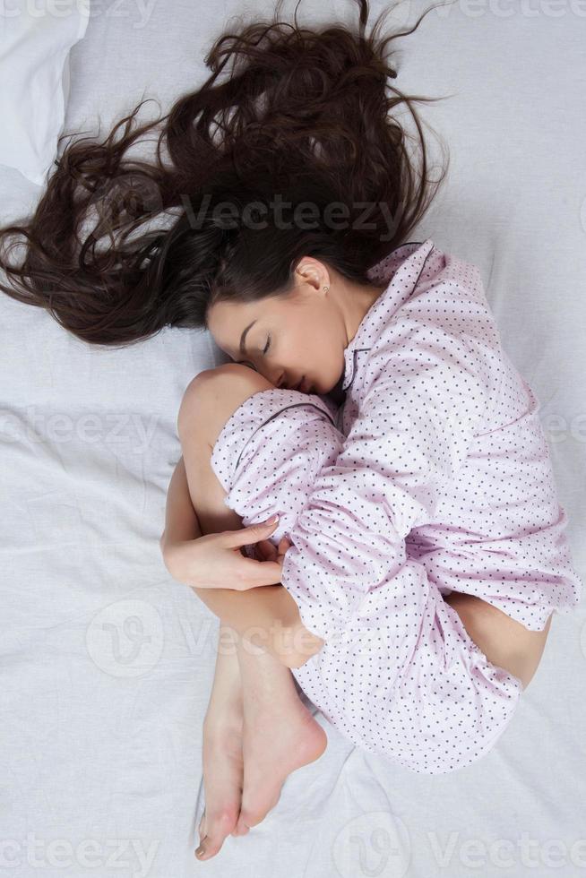 Girl sleeps in a white bed at home. Young woman sleeping in sleepwear on the white linen in bed at home, top view. photo