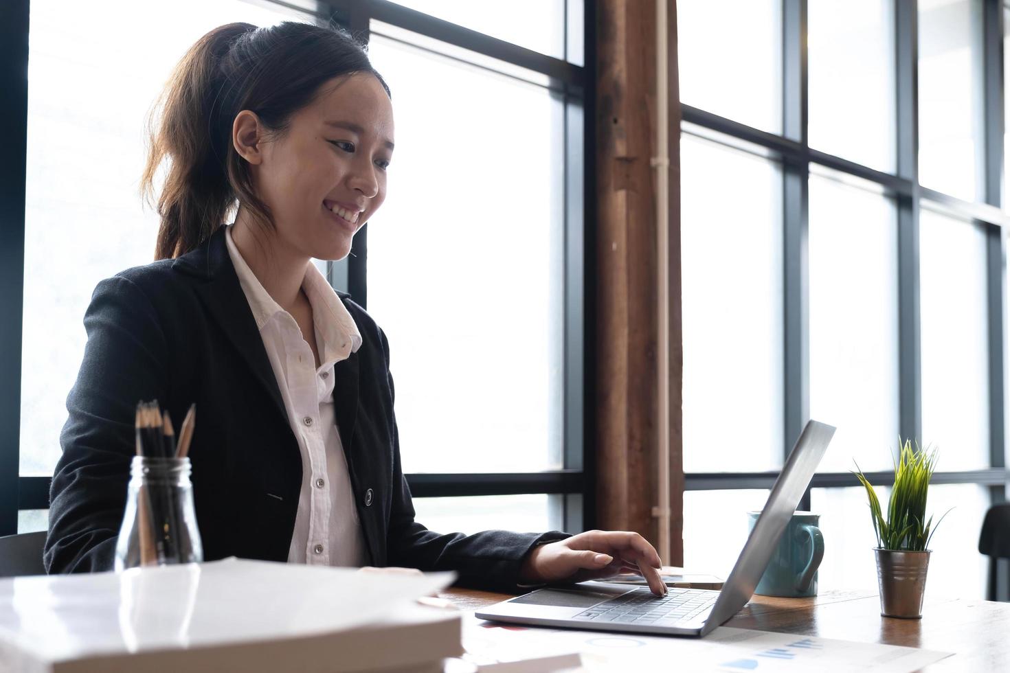 Beautiful young asian woman sitting at coffee shop using laptop. Happy young businesswoman sitting at table in cafe with tab top computer. photo