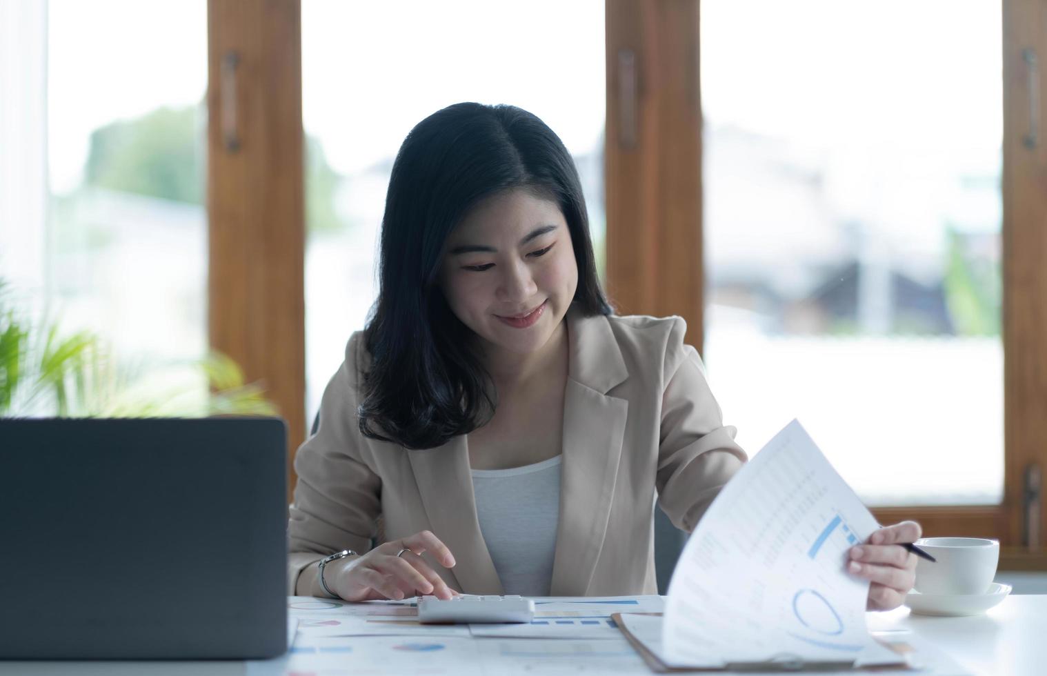 Asian Businesswoman using a calculator and laptop computer for doing math finance on a wooden desk, tax, accounting, statistics report and analytical research concept. photo