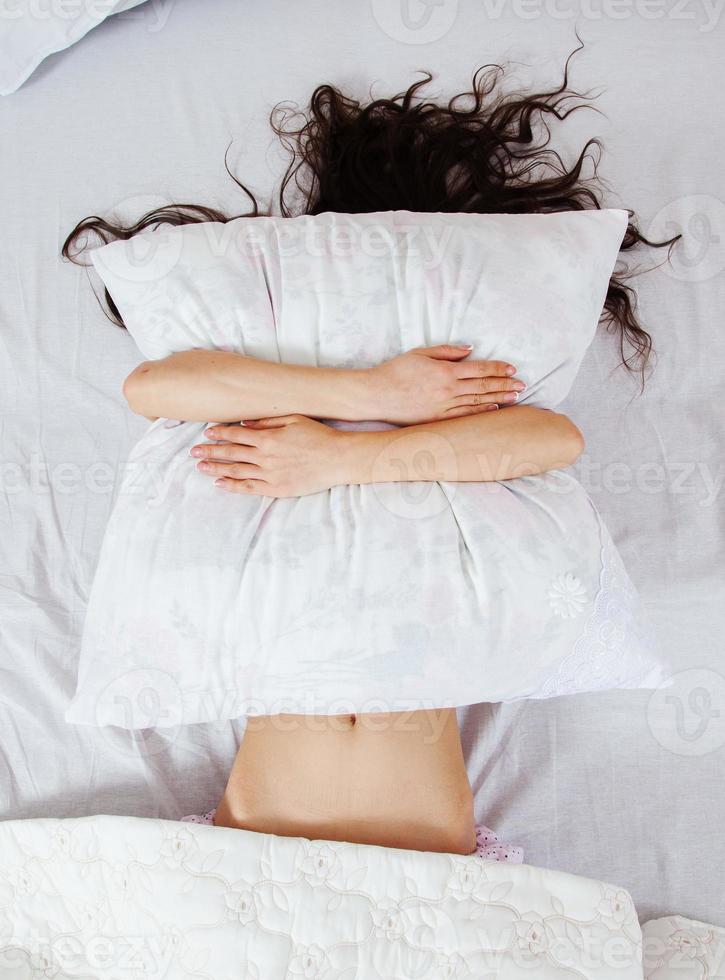 chica duerme en una cama blanca en casa. mujer joven durmiendo en ropa de dormir en el lino blanco en la cama en casa, vista superior. foto