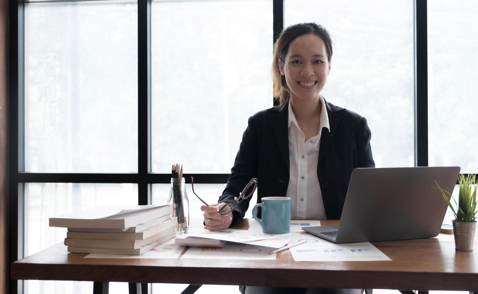 encantadora mujer asiática que trabaja en la oficina usando una laptop mirando la cámara. foto