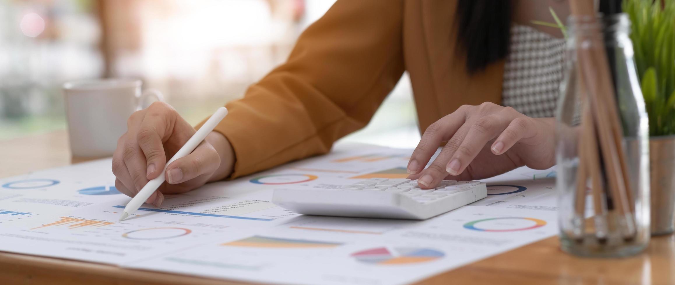 Business woman using calculator to calculate financial report, working at office with laptop computer on table. Asian female accountant or banker making calculations. finances and economy concept photo