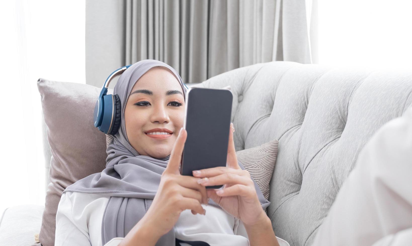 Close-up image, Attractive Muslim woman using a smartphone in living room, chatting with her friends or scrolling on online shopping website. photo