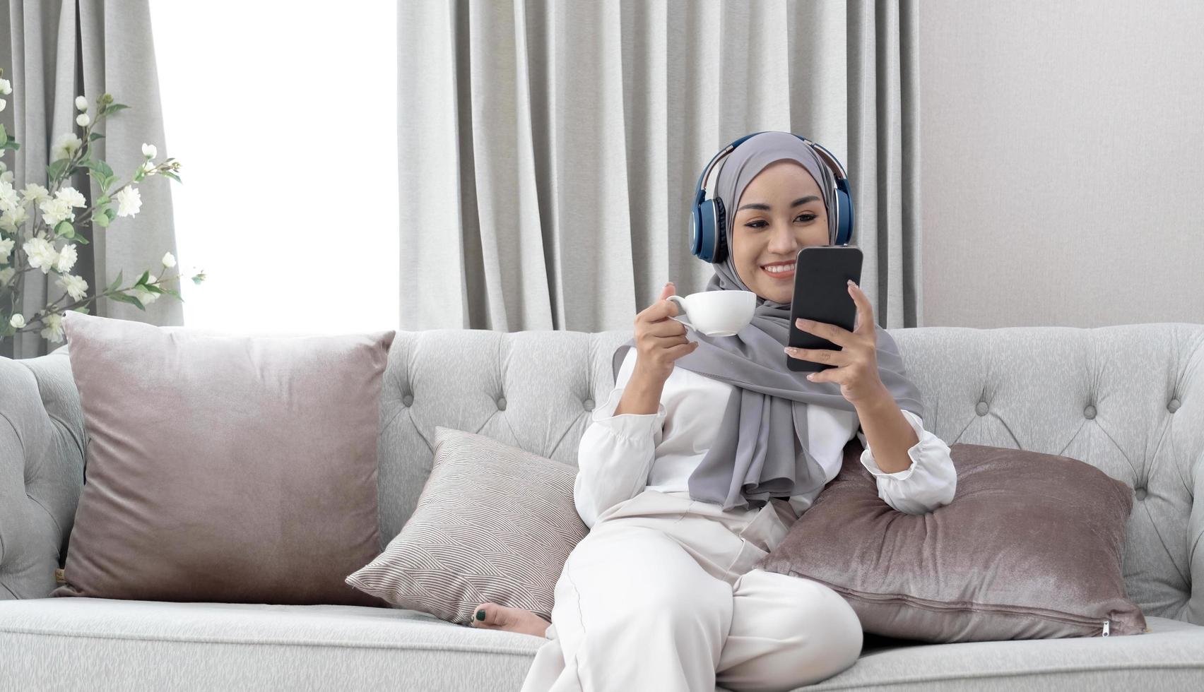 Attractive young Muslim woman sitting in living room, using smartphone and laptop computer. cropped image photo
