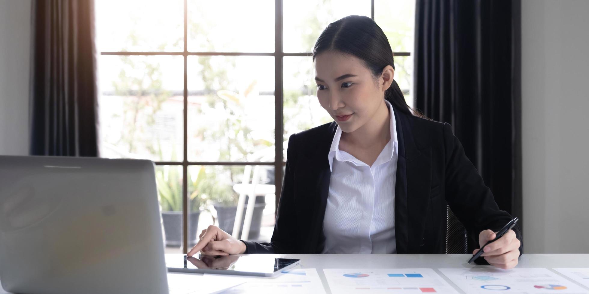 Portrait of Young Asian woman hand freelancer is working her job on computer tablet in modern office. Doing accounting analysis report real estate investment data, Financial and tax systems concept. photo