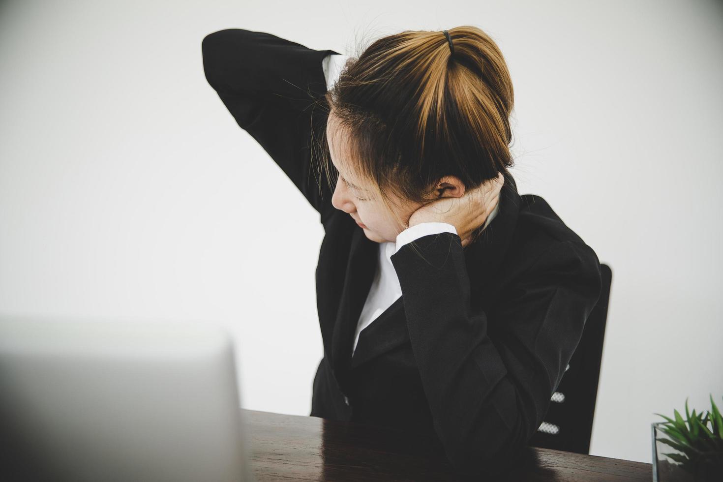 una joven asiática está sentada en el trabajo y tiene dolor en el cuello foto