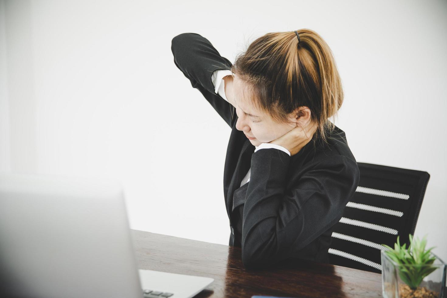 Young asian woman is sitting at work and has pain in her neck photo