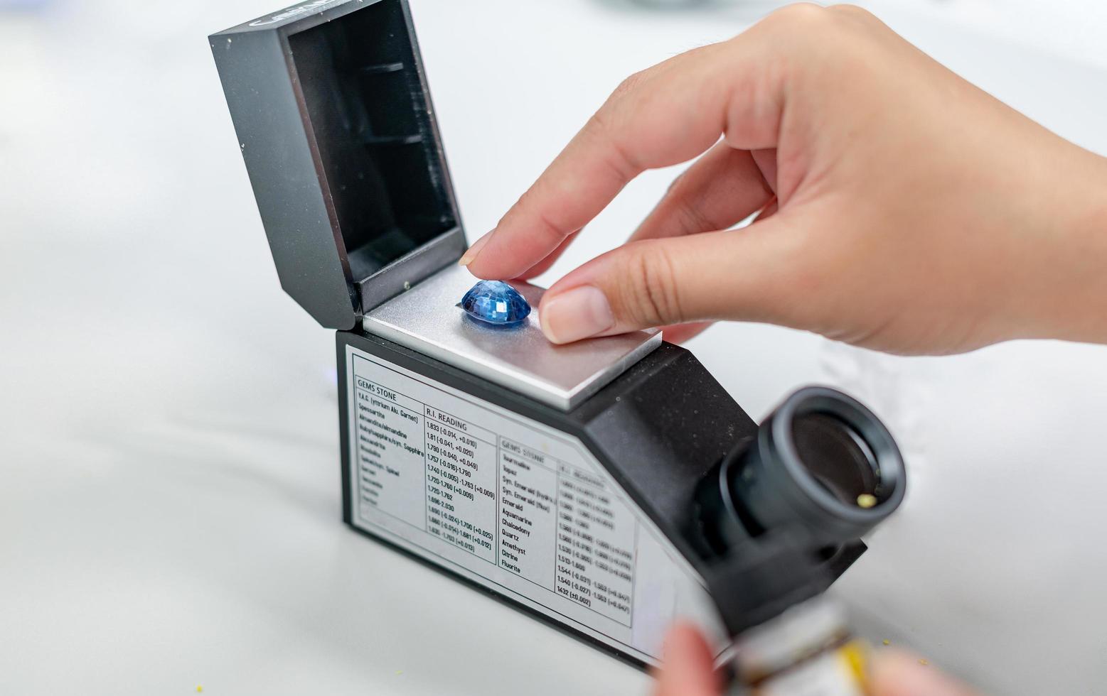 Female hand holding the blue precious stone and put on the refractometer for confirm the type of stone photo