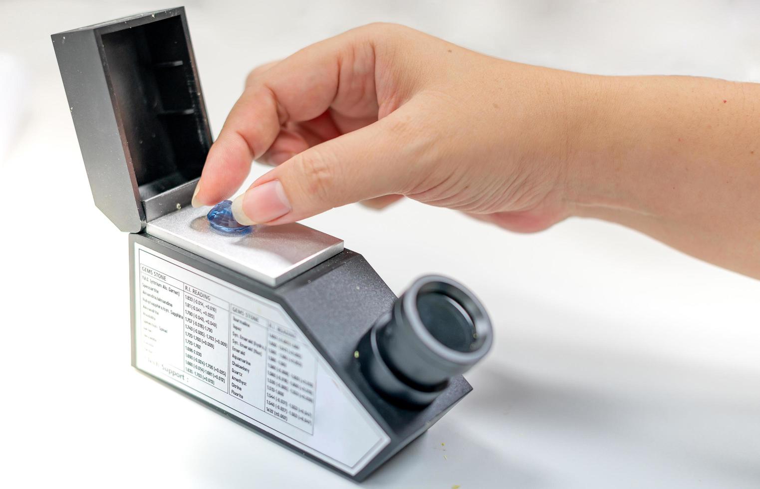 Female hand holding the blue precious stone and put on the refractometer for confirm the type of stone photo