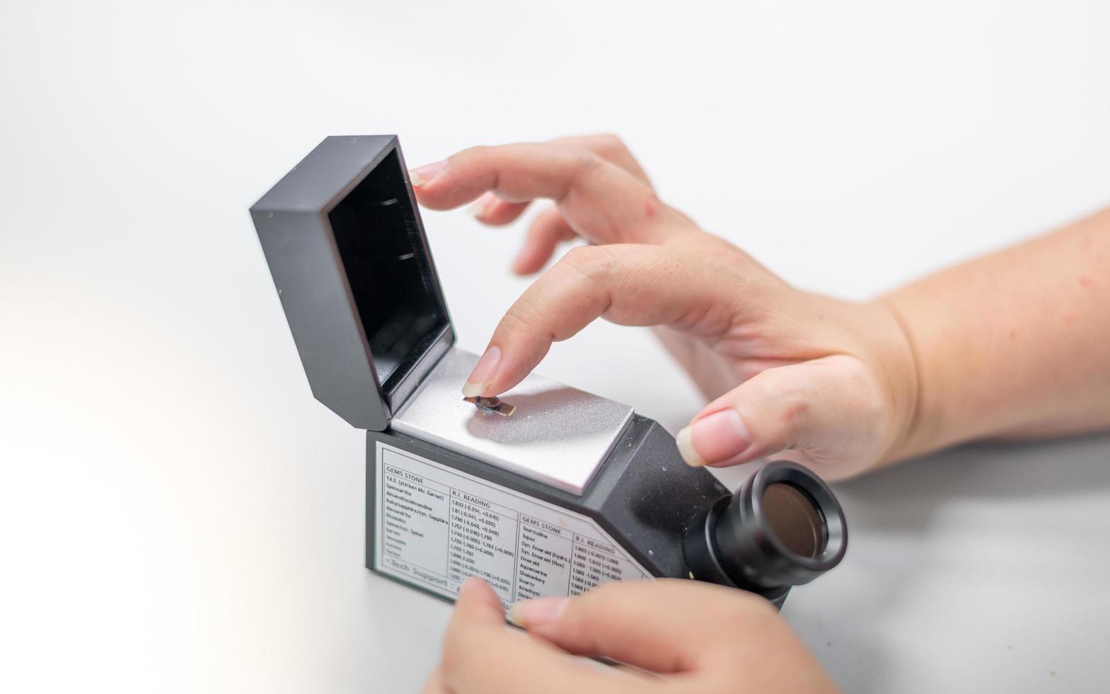 Female hand holding the precious stone for checking the specific of the type of precious stone  with the refractometer equipment. photo