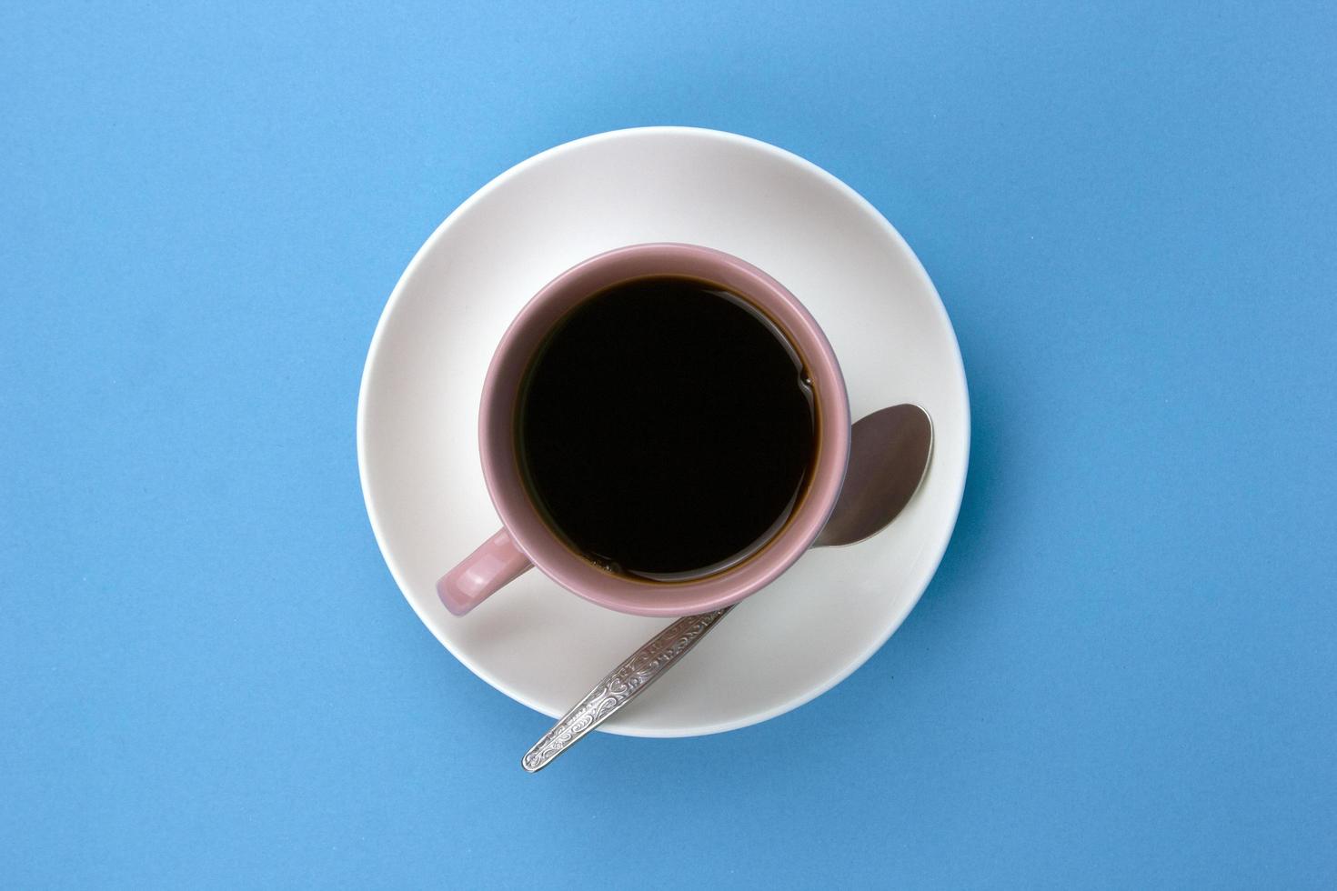 An isolated black coffee on light pink cub on blue background with small spoon photo