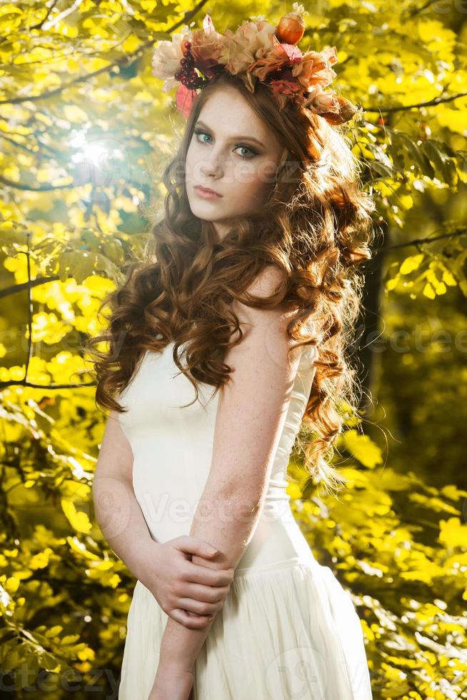 Young woman holding a bunch of yellow maple leaves. Autumn portrait of young woman. Red haired girl in autumn forest photo