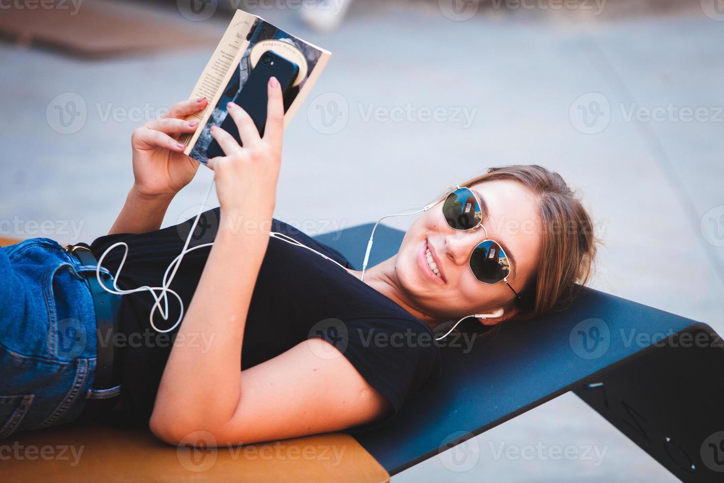 Photo of a cheerful smiling cute young student girl wearing sunglasses outdoors using mobile phone chatting listening music with earphones.