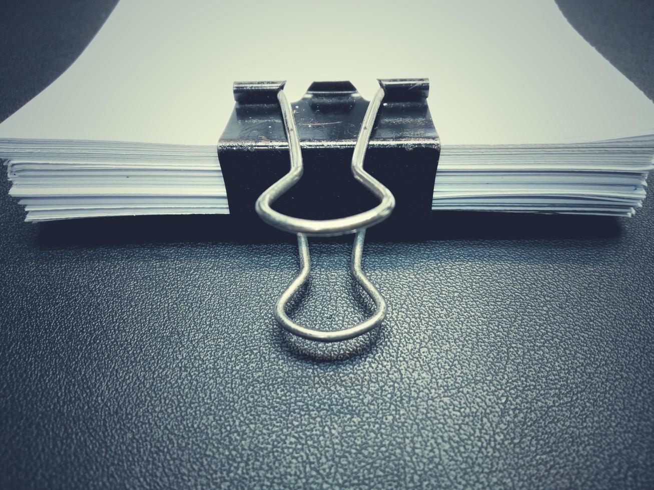 The black clip, white paper clip. Placed on a black surface with dark edges of the desk. photo