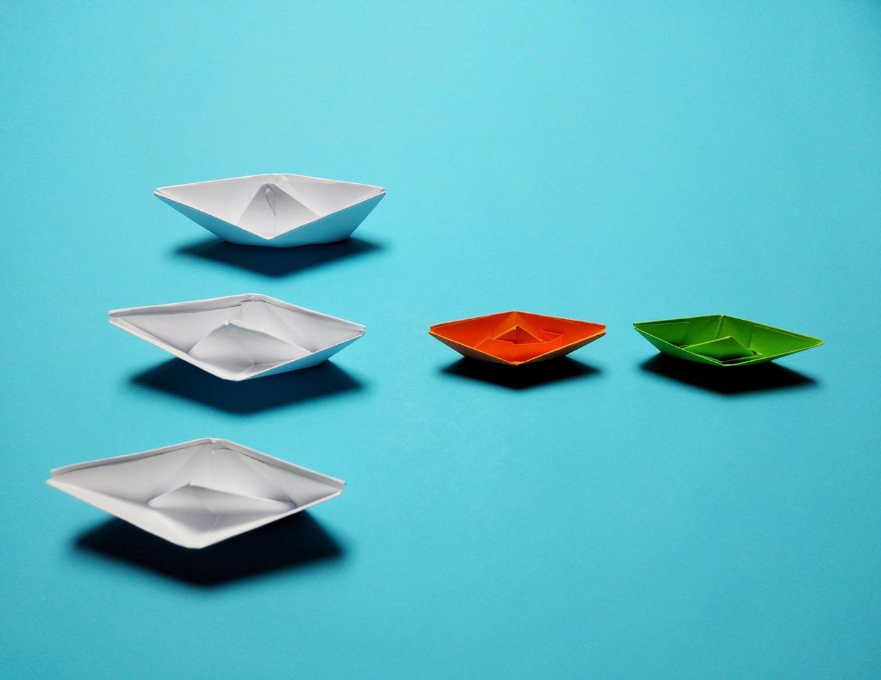 Green-orange-white paper boats on a blue background give the concept of leadership and high-efficiency management a sense of solidarity, unity, love, unity, success. photo