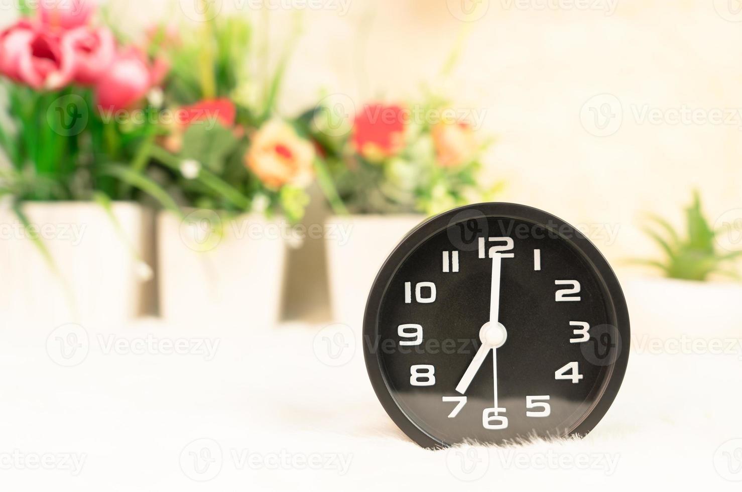 Black alarm clock and flower in vase on table photo