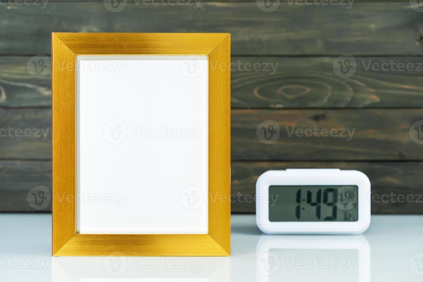 Blank golden frame and digital alarm clock on table photo