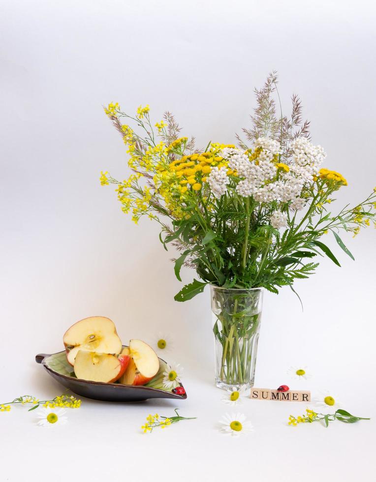 bodegón de flores silvestres y una manzana en un platillo, todo sobre un fondo claro foto