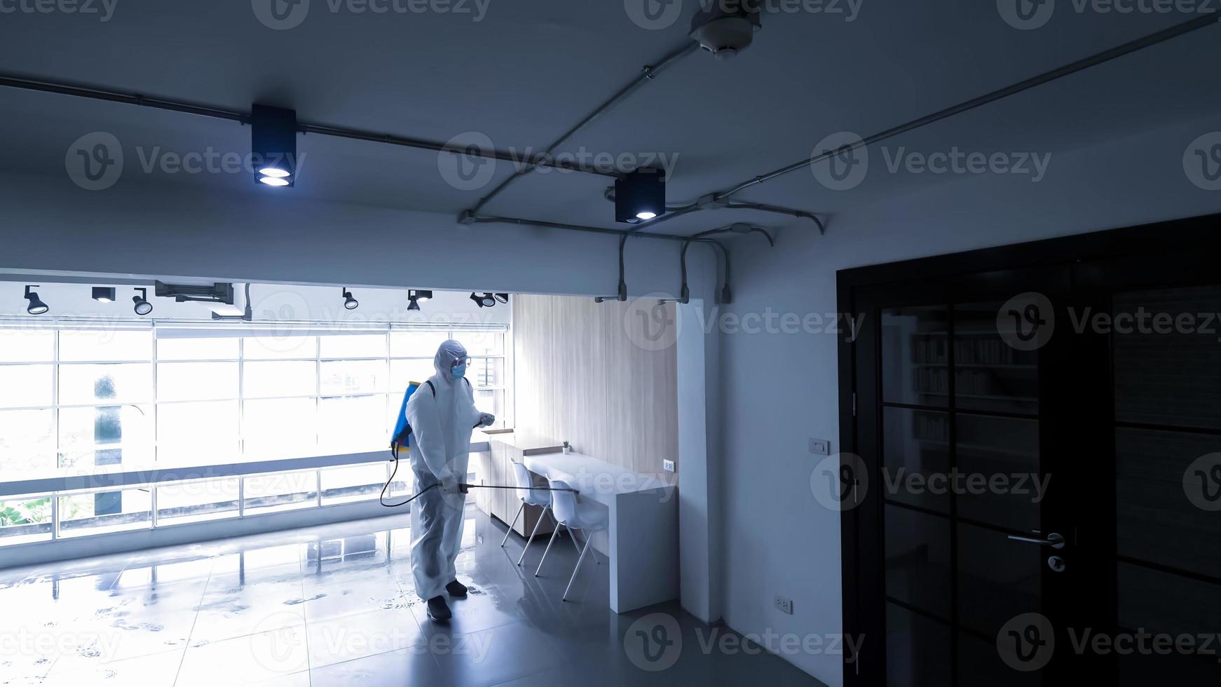 Worker in personal protective equipment suit cleaning in building with spray disinfectant water to remove covid 19 photo