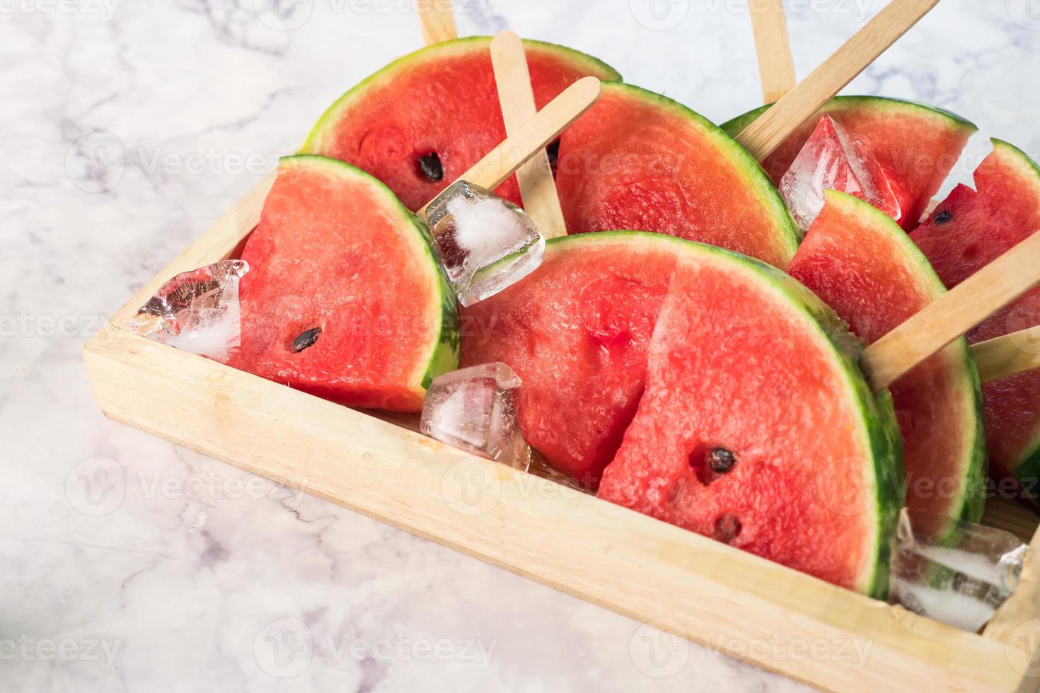 Watermelon slices on sticks with ice cubes. Fresh watermelon popsicles in wooden bowl. photo