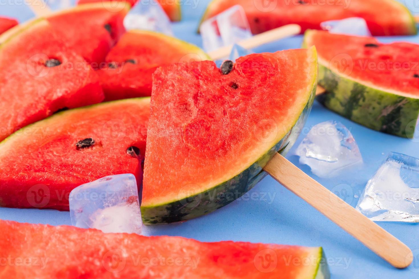 Watermelon slices on sticks with ice cubes. Fresh watermelon popsicles on blue background. photo