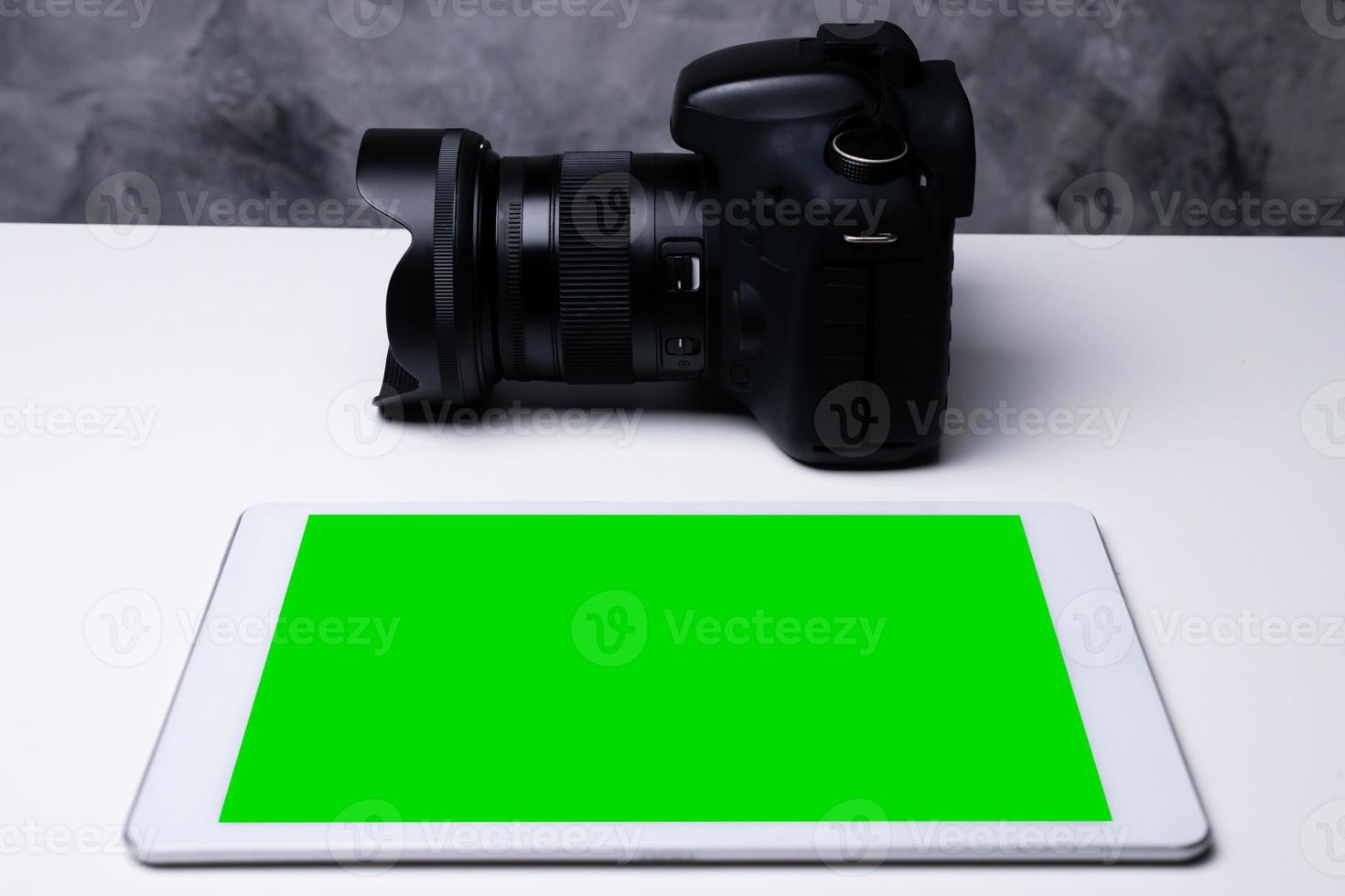 A black digital camera and a blank screen tablet on a table. photo