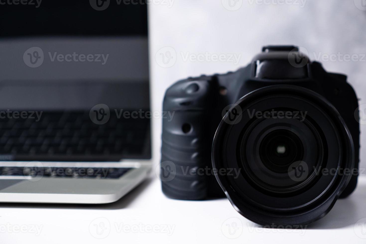 A black digital camera and a computer laptop on a table. photo