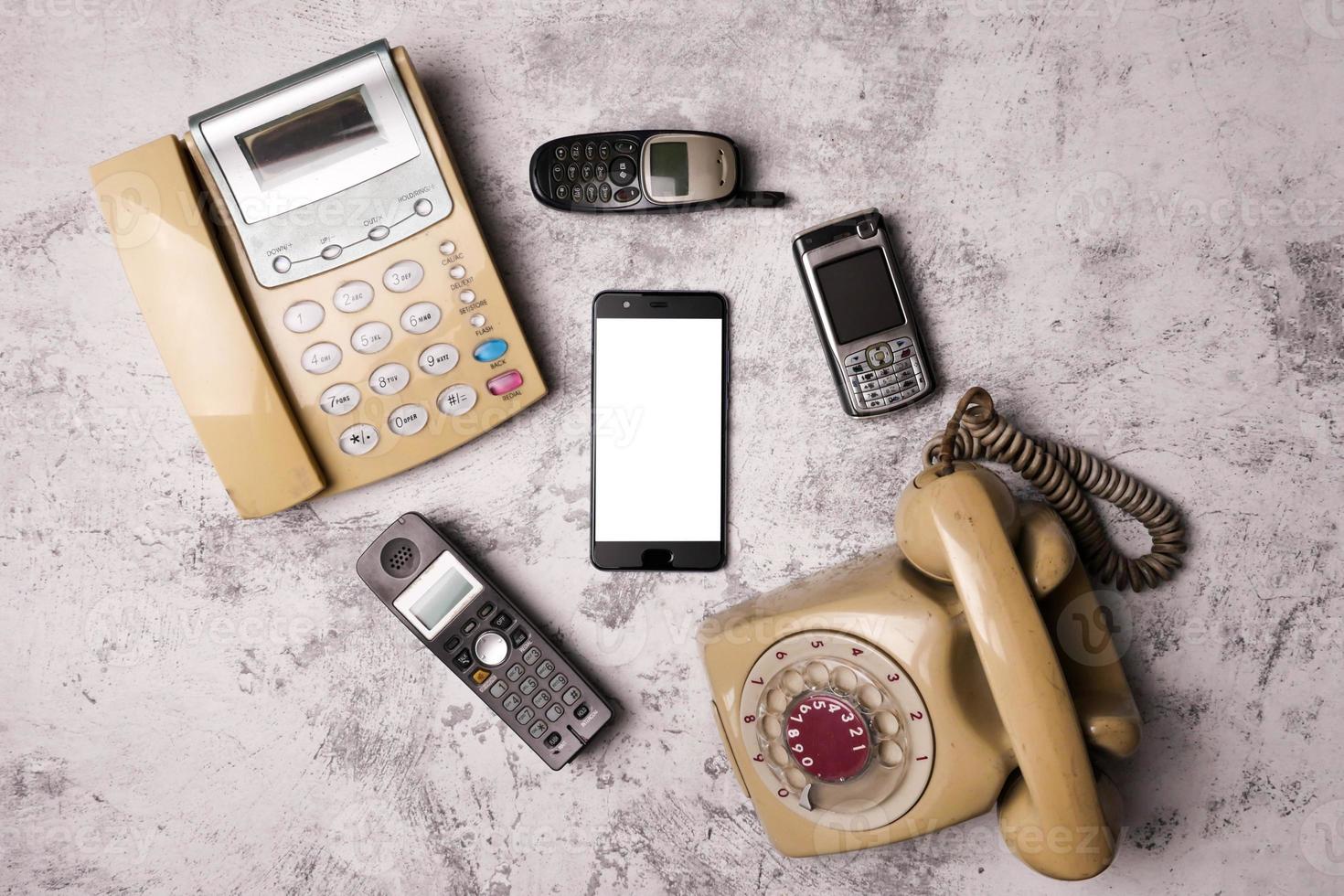 An old telephone with rotary dial, a landline, an obsoleted cellphone and smartphone on a grunge background. photo