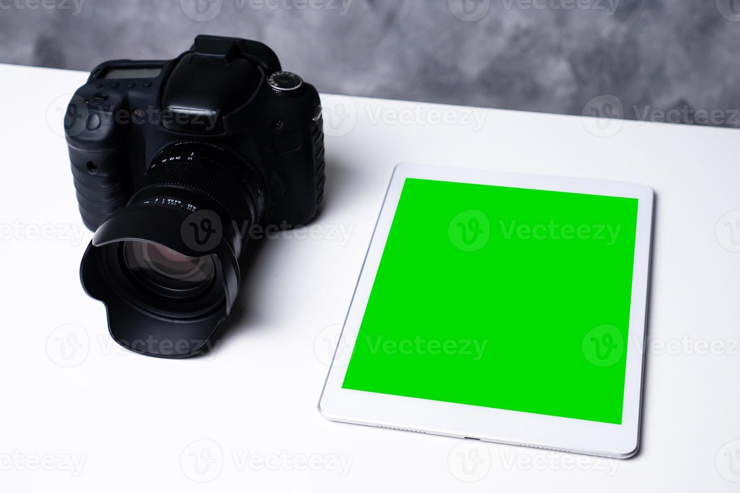 A black digital camera and a blank screen tablet on a table. photo