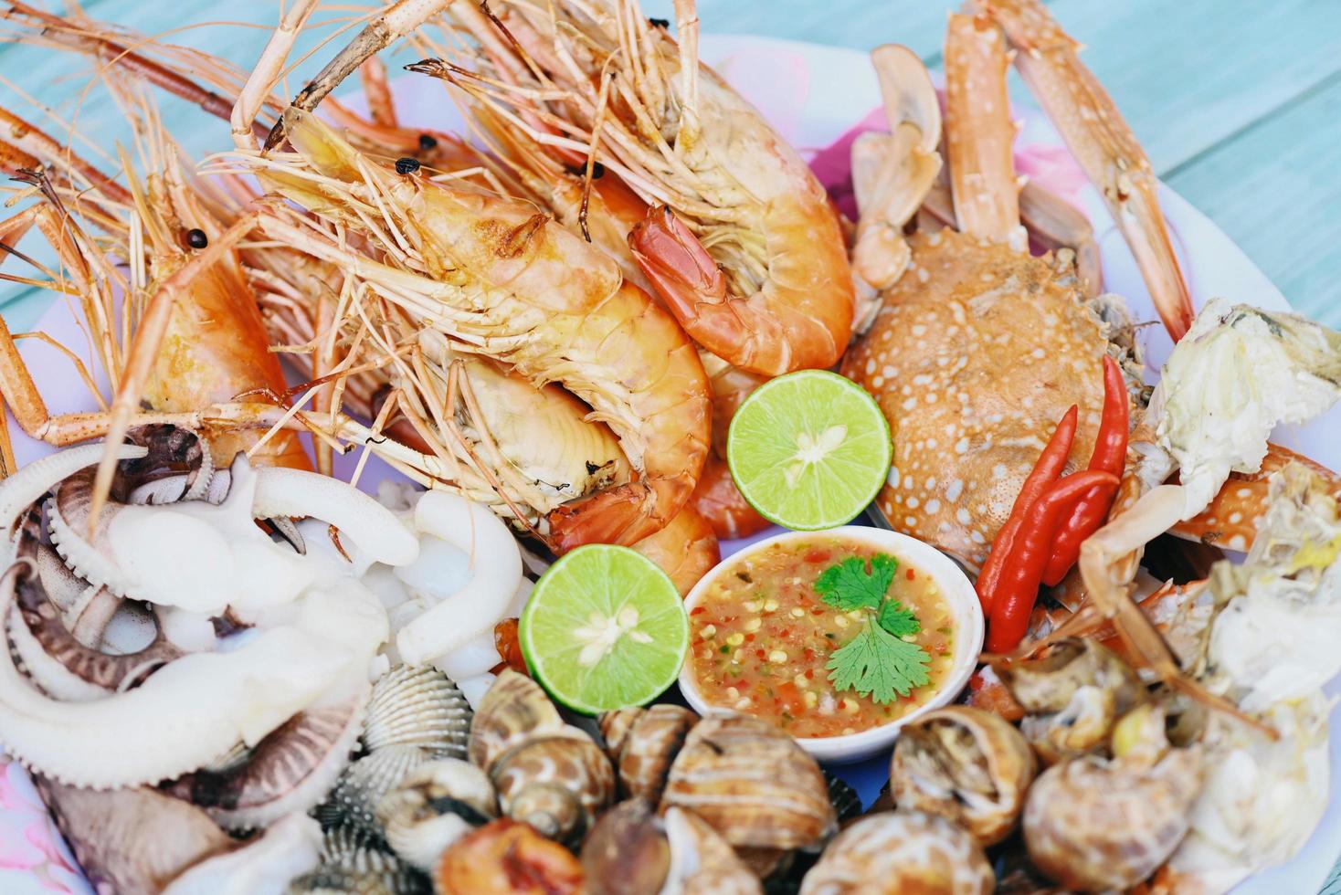 seafood plate with shrimp shellfish crab squid cockle spotted babylon with seafood sauce chili lemon lime serve on dining table, shrimps prawns seafood buffet menu cooked food photo