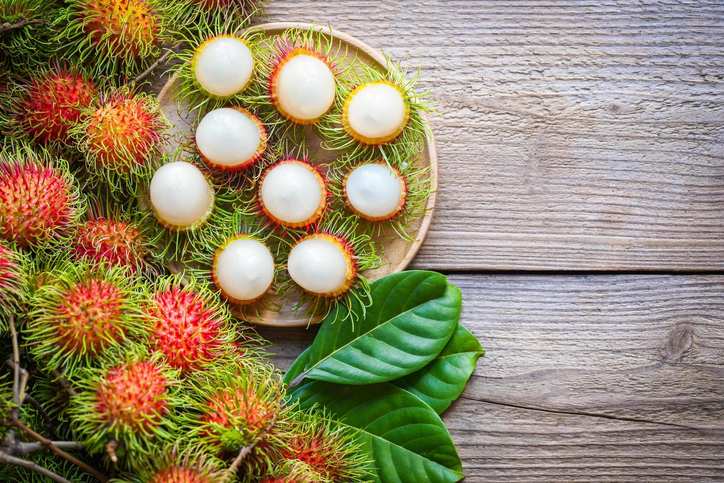 rambután fresco y maduro fruta tropical dulce rambután pelado con hoja, fruta de rambután en plato y cosecha de fondo de madera del árbol de rambután en el jardín - vista superior foto