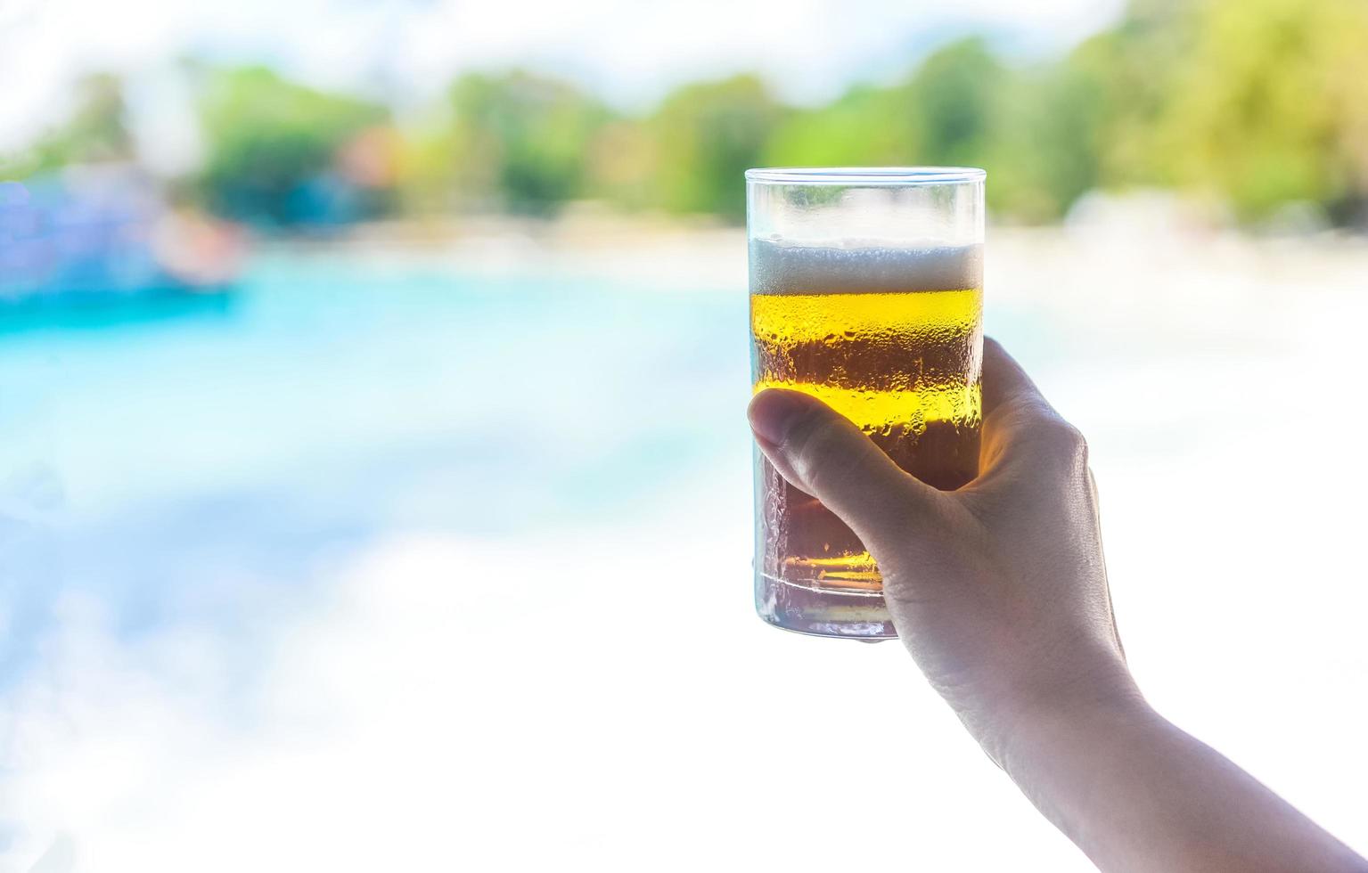 Beer mug in hand with sea background - hand holding a mug of beer on beach in summer hot weather ocean landscape nature outdoor vacation photo