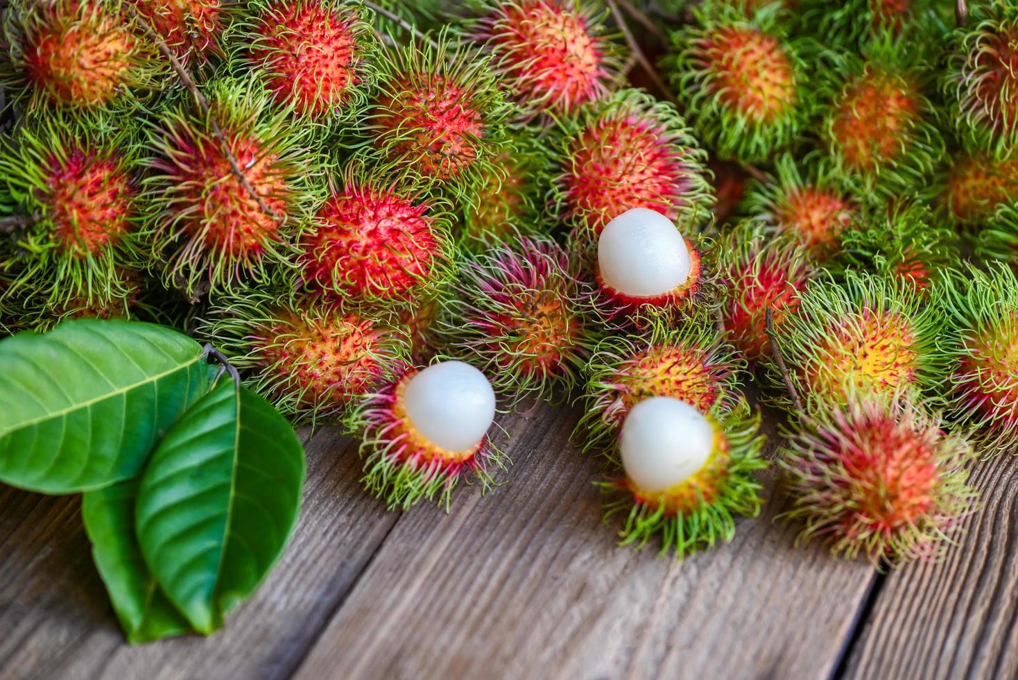 fruta de rambután sobre fondo de madera cosecha del árbol de rambután del jardín, rambután dulce de fruta tropical fresca y madura rambután pelado con hoja foto