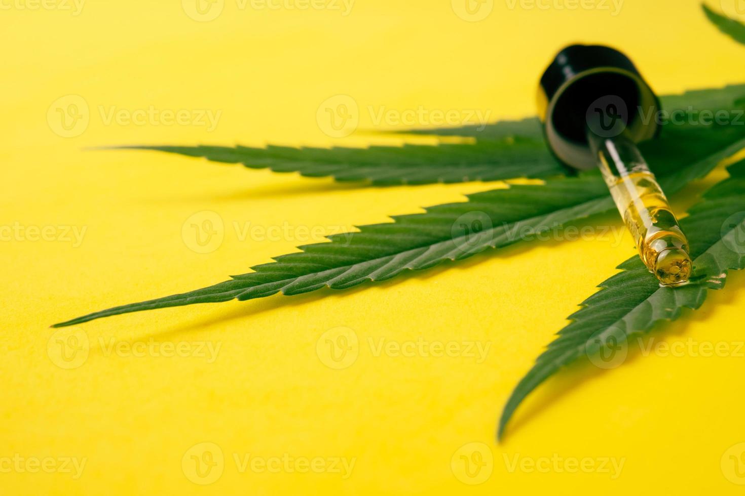 Cannabis oil in the dropper tube with green leaf on yellow background. Alternative medicine concept. photo