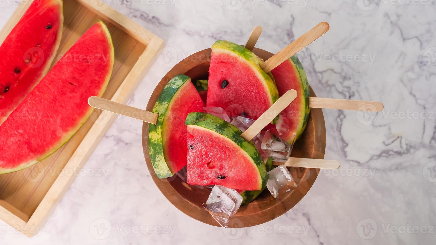 Watermelon slices on sticks with ice cubes. Fresh watermelon popsicles in wooden bowl. photo
