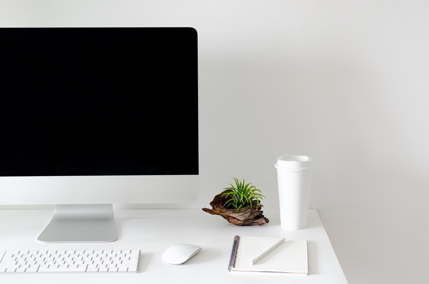 pantalla de computadora personal moderna en mesa blanca con una taza de café y planta de aire tillandsia con espacio para texto en pared blanca para trabajo y concepto de oficina. foto