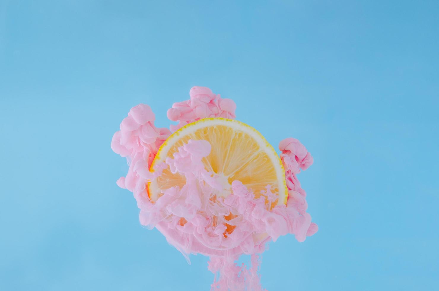 Slice lemon with partial focus of dissolving pink poster color in water on blue background for summer, abstract and background concept. photo