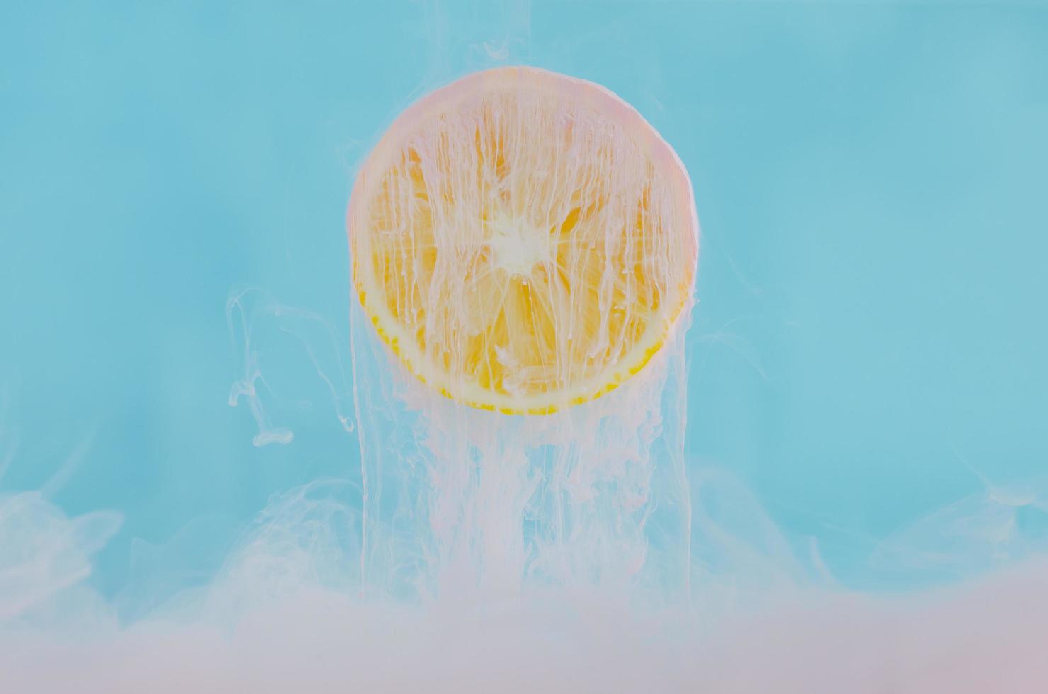 Blurred focus of dissolving pink poster color in water with slice lemon on blue background for summer, abstract and background concept. photo