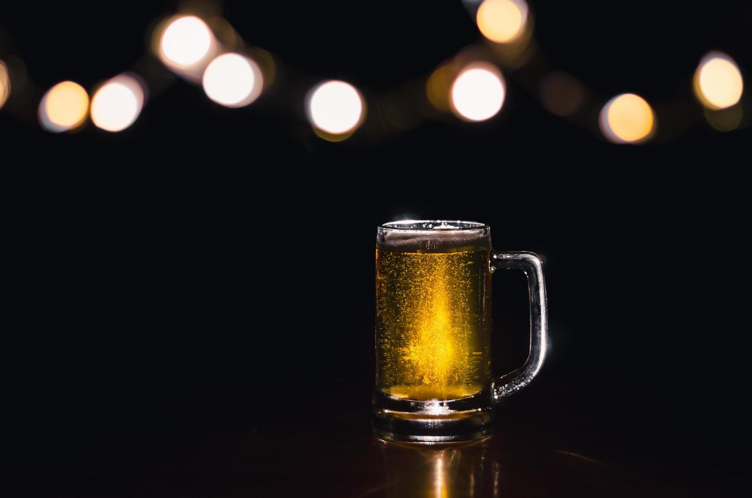 un vaso de cerveza sobre una mesa de madera que tiene luces bokeh en la parte superior con un fondo oscuro. foto