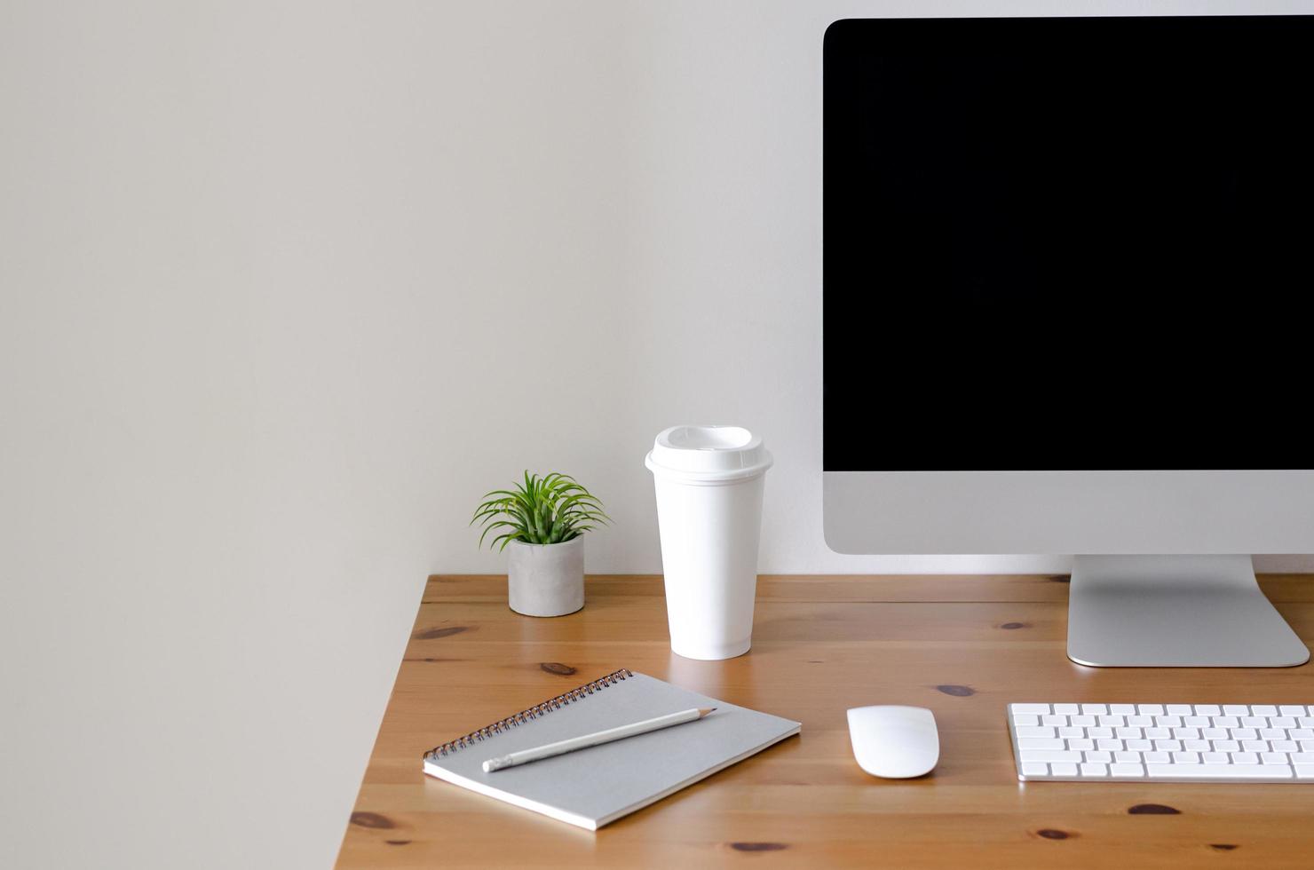 Modern personal computer screen on wooden table with a cup of coffee and Tillandsia air plant with space for text on white wall for working and office concept. photo