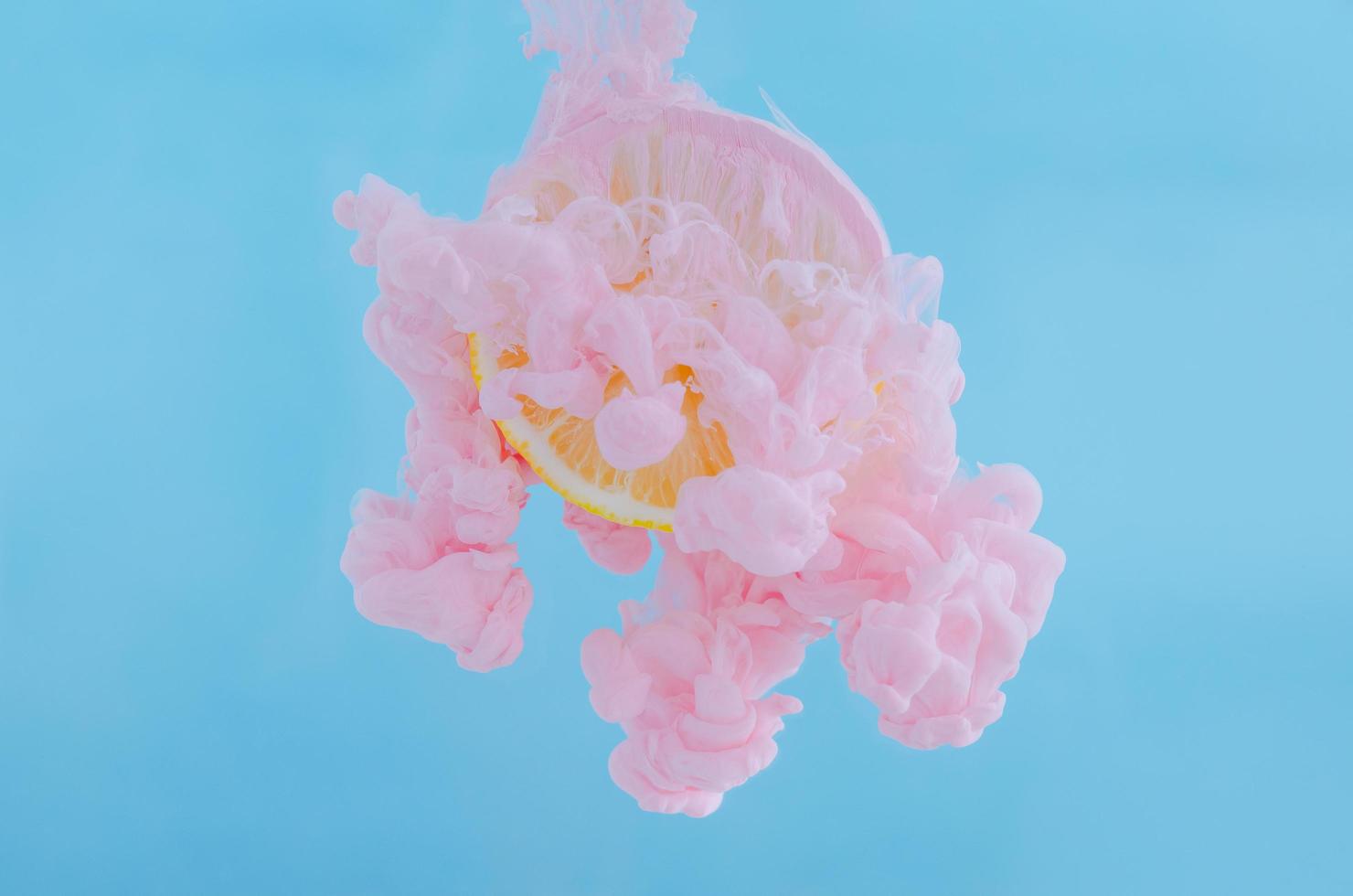 Slice lemon with partial focus of dissolving pink poster color in water photo